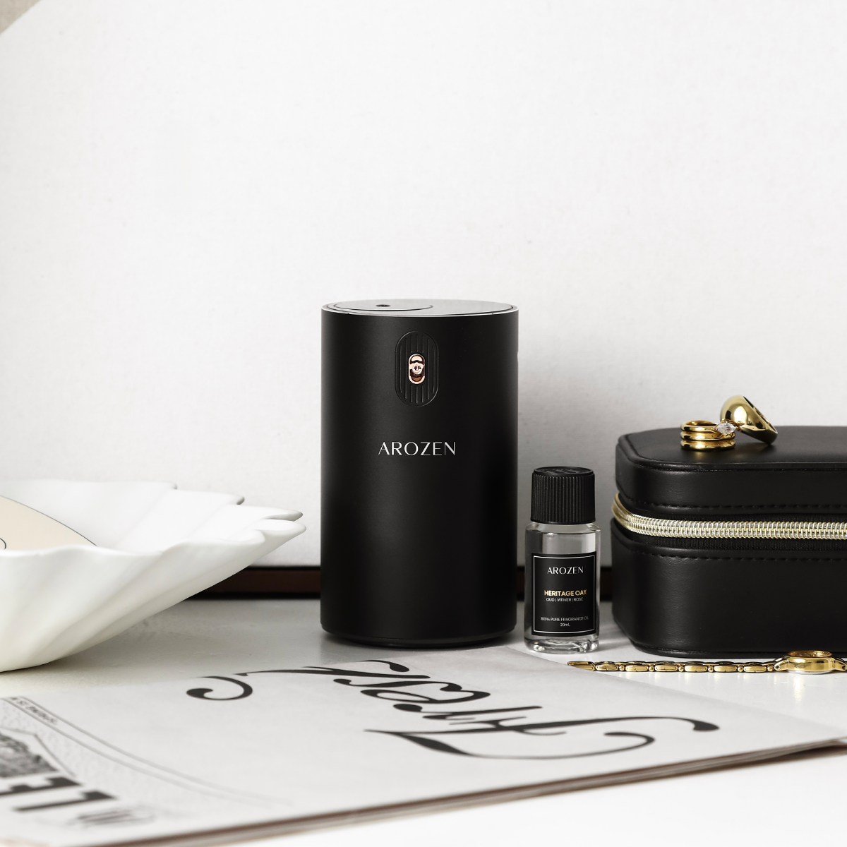 A sleek black cylindrical EON MINI ELECTRIC SCENT DIFFUSER by Arozen stands on a table next to a fragrance oil bottle with some jewelry —all arranged in minimalist style.