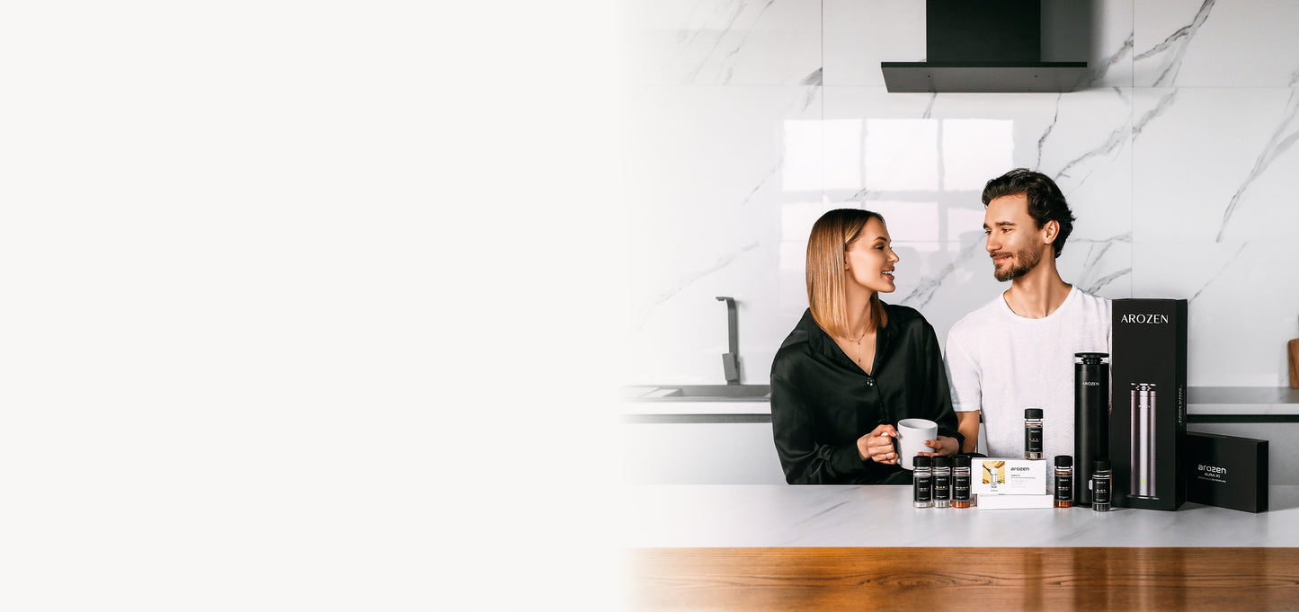 A woman and man sit at a modern kitchen counter with various electric scent diffuser products displayed in front of them. They are smiling at each other and appear relaxed, with a sleek kitchen backdrop and marble wall behind them.