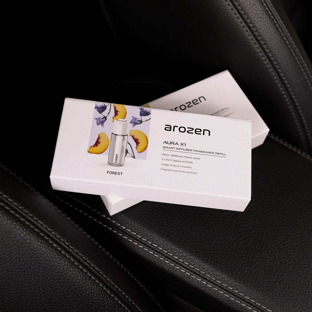Two white Arozen FOREST - AURA X1 FRAGRANCE OIL REFILL boxes sit on black leather car seats. Ideal for a fresh forest car scent, the front box features a diffuser image and soft peach illustrations.